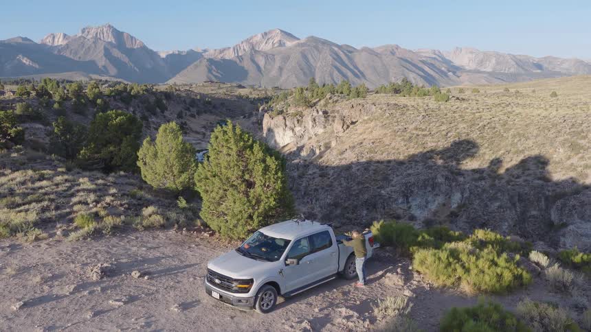 An adventurer parks his pickup truck at a scenic overlook in the mountains and prepares his camera gear to film the stunning canyon below