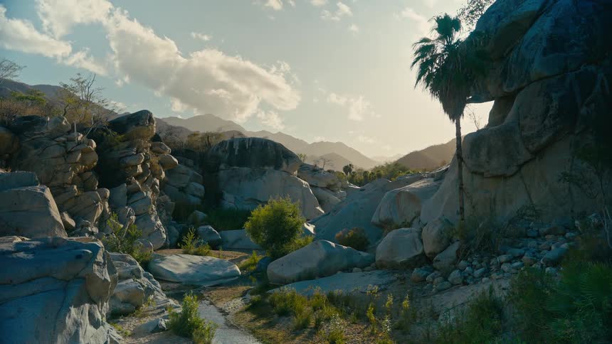 A beautiful time-lapse of a tranquil stream flowing through a rocky desert canyon with mountains in the background at golden hour