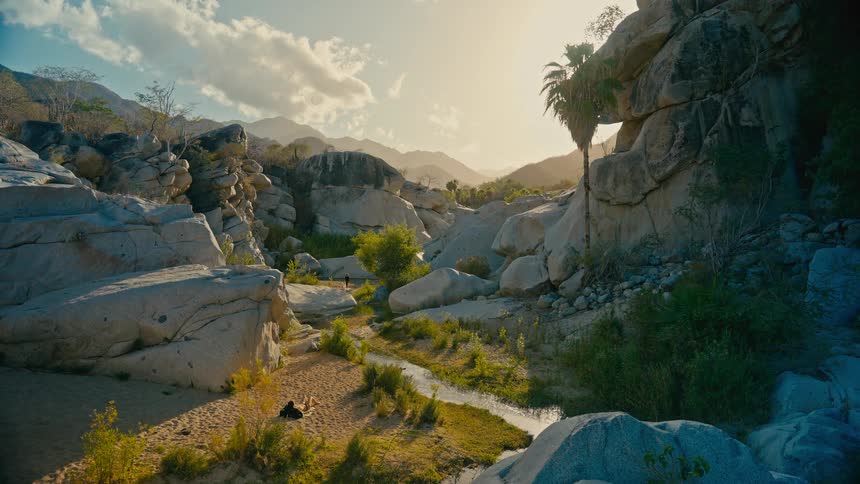 A majestic rocky canyon oasis with a winding stream glows in the warm light of the setting sun