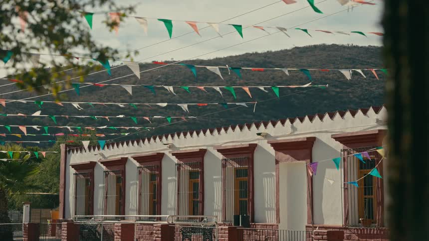 Colorful festive pennant flags gently sway in the breeze in front of a colonial-style building with a mountain backdrop