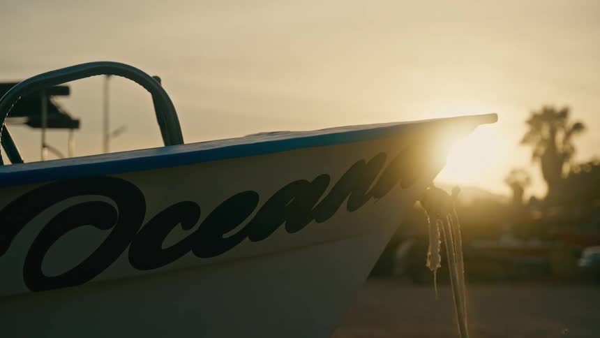 Close up of a boat named 'Ocean' docked on a tropical shore as the sun sets in the background
