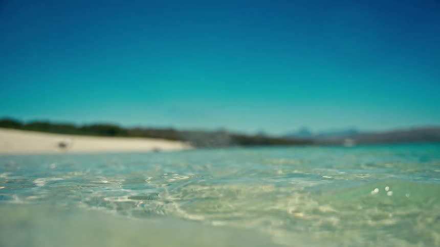 A serene low-angle view of crystal clear ocean water gently lapping at the shore of a beautiful tropical beach under a clear blue sky