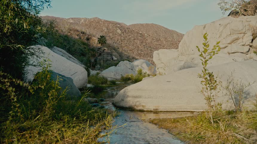 A serene stream flows gently through a rocky canyon in a tranquil desert mountain landscape