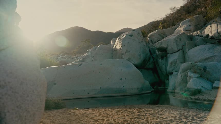 A tranquil desert canyon oasis with a still pool of water surrounded by large rocks glows in the warm morning sun