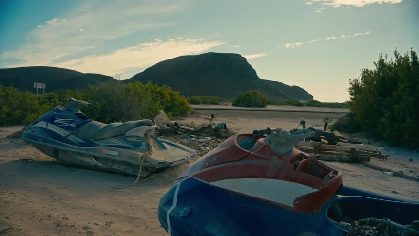 A static shot of two abandoned and broken jet skis sitting on a sandy patch in a desolate coastal landscape