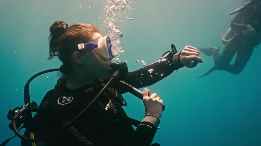 A female scuba diver checks her dive computer while floating serenely underwater in slow motion