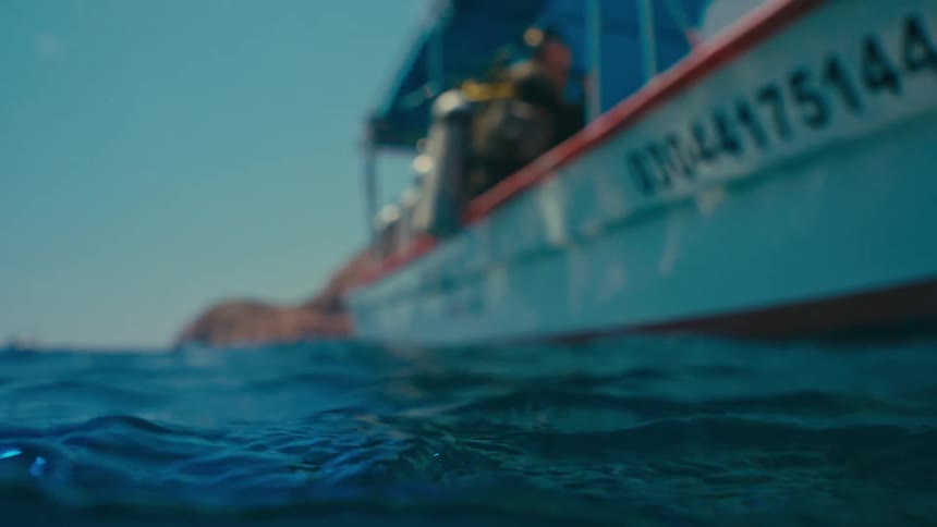 A tranquil slow-motion split-level view captures the gentle motion of the ocean surface with a dive boat waiting in the background