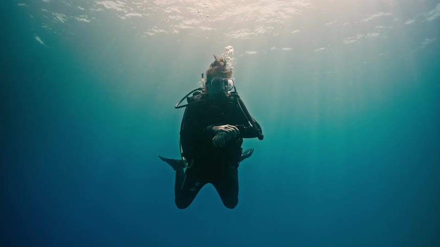 A female scuba diver floats serenely in the deep blue ocean as sun rays beam down from the surface