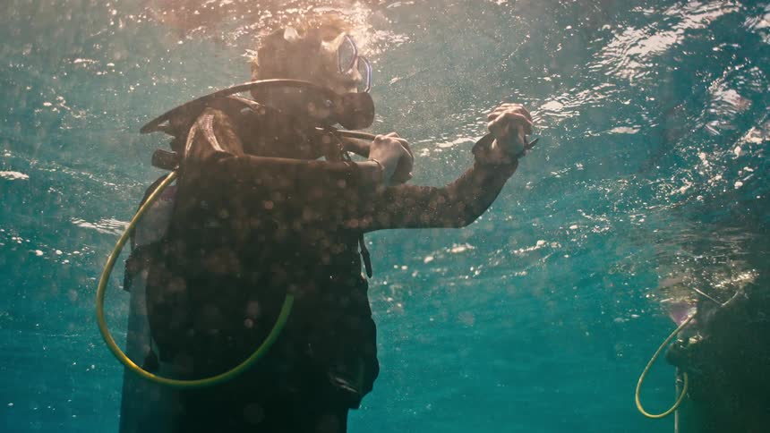 A scuba diver floats serenely just below the ocean's surface as sunlight filters through the water in slow motion