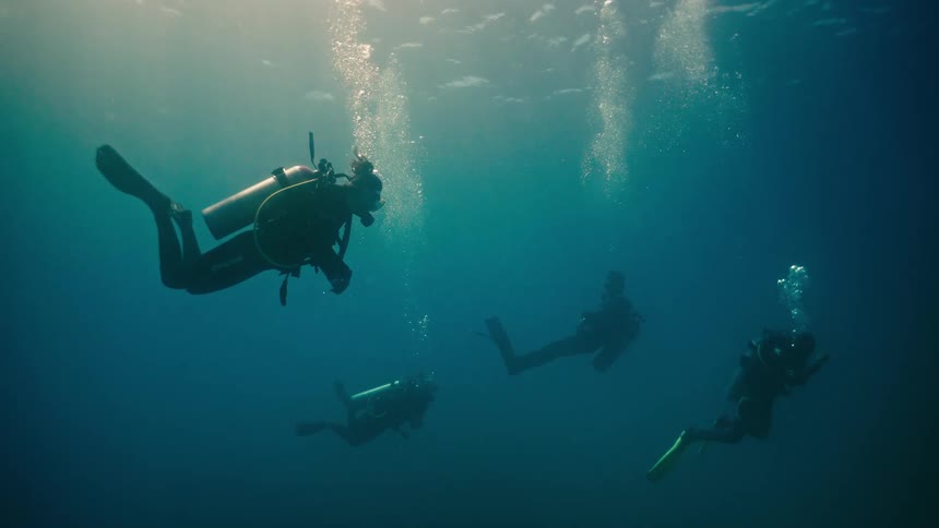 A cinemagraph of four scuba divers floating serenely in the deep blue ocean as bubbles rise to the sunlit surface
