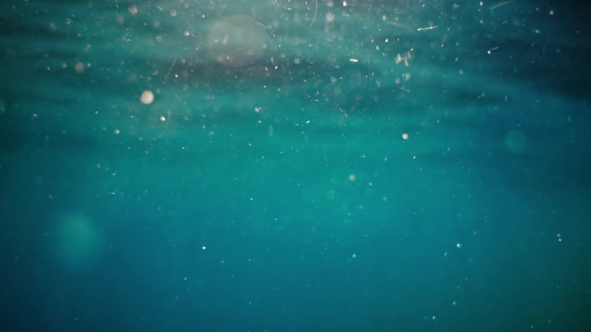 Serene underwater scene with shimmering light rays illuminating tiny particles floating in the deep turquoise water