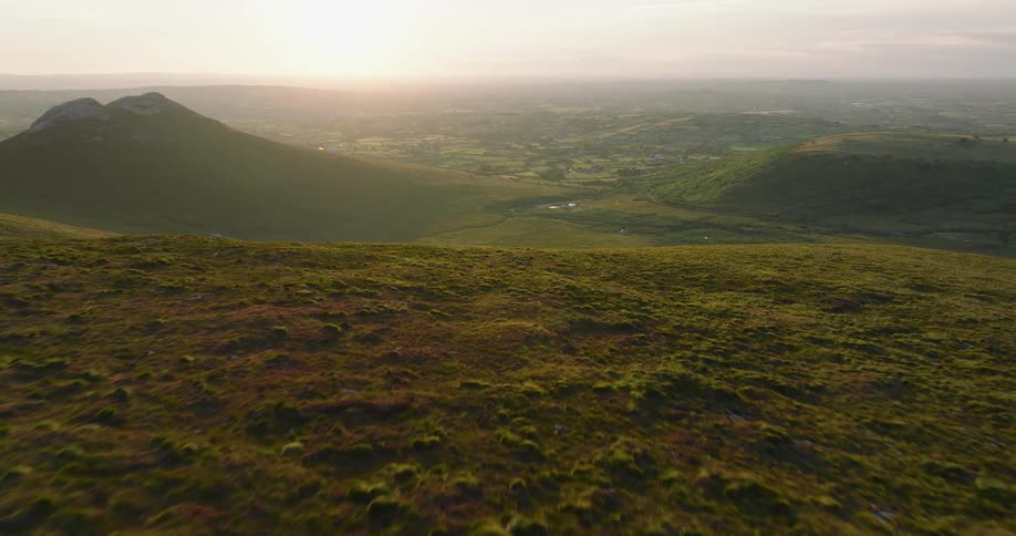Cinematic aerial footage soars over a verdant hillside, revealing a sprawling rural valley bathed in the warm light of sunset