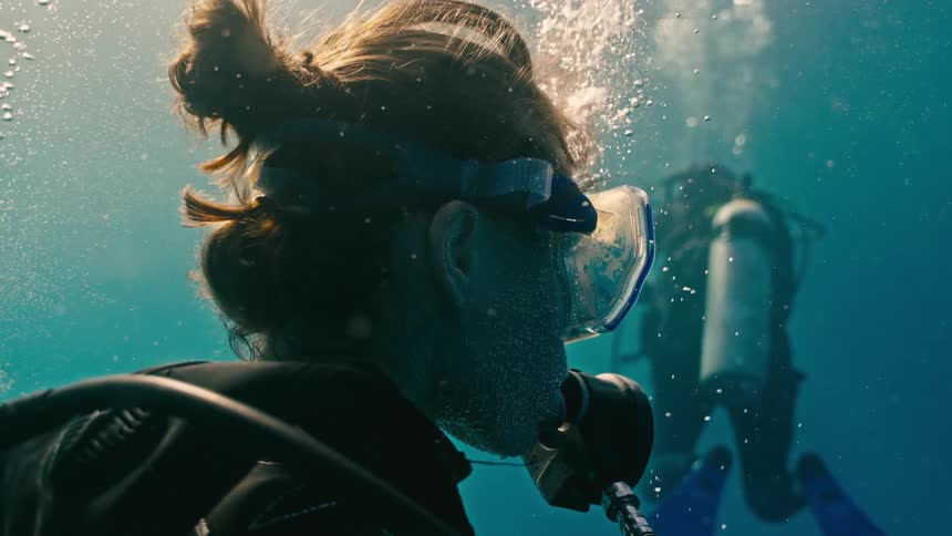 Dramatic slow-motion close-up of a female scuba diver breathing underwater as the camera pans from her profile to her back
