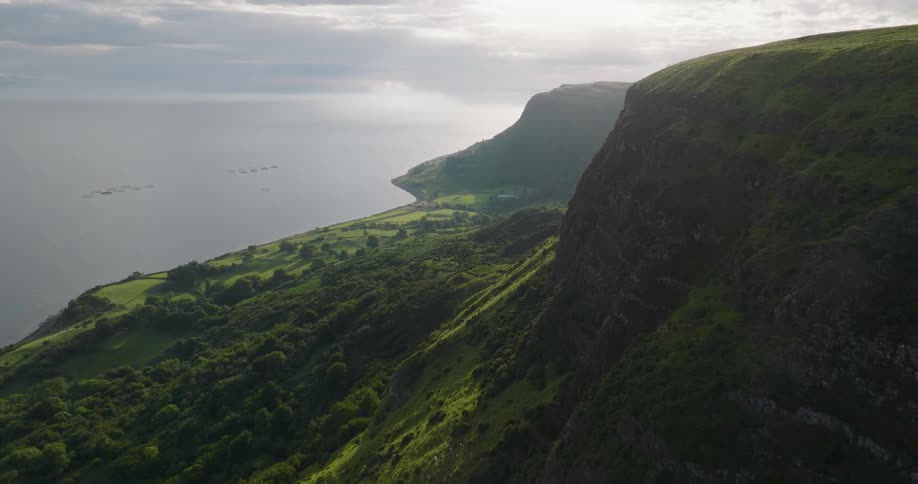 A breathtaking aerial journey along a verdant, sun-kissed coastline featuring towering cliffs and a tranquil sea
