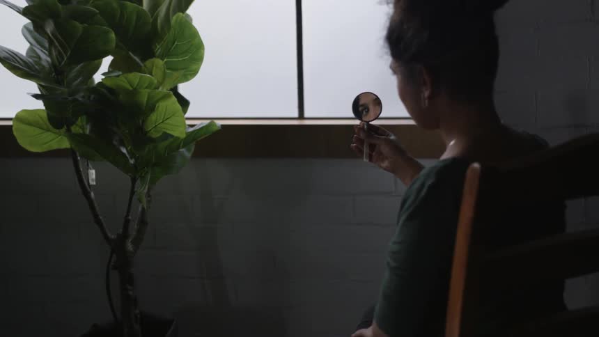 A woman looks at her reflection in a small hand mirror