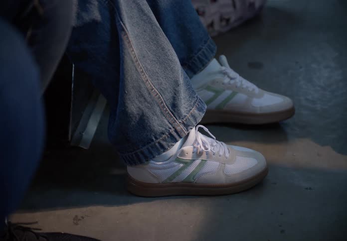 A close-up shot of a person's feet in white and green sneakers and blue jeans, tapping slightly on the floor