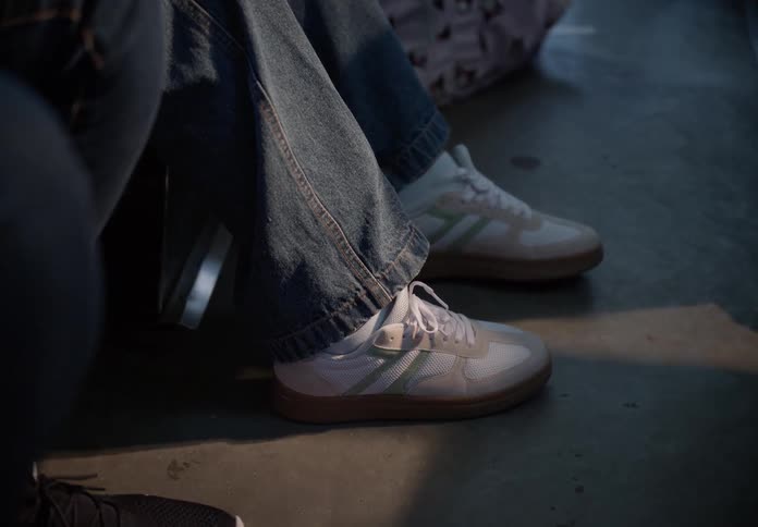A static close-up shot of a person's feet in white sneakers with green stripes, possibly on public transport
