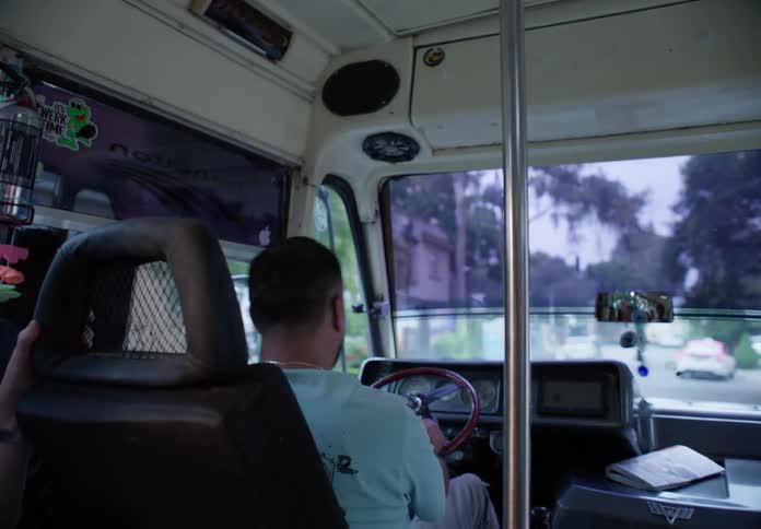 A view from behind the driver of a city bus as he navigates through traffic
