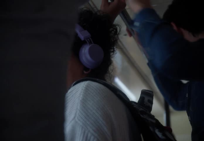 A contemplative woman with glasses and headphones stands on a crowded bus during her daily commute