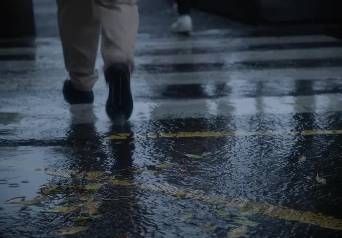 A person's legs in slow motion walking away on a wet city street during a rainstorm as a car drives past