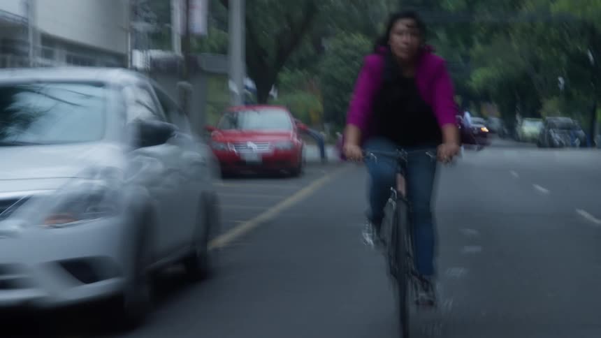 An experimental, shaky, and blurry shot follows a woman as she rides her bicycle down an urban street
