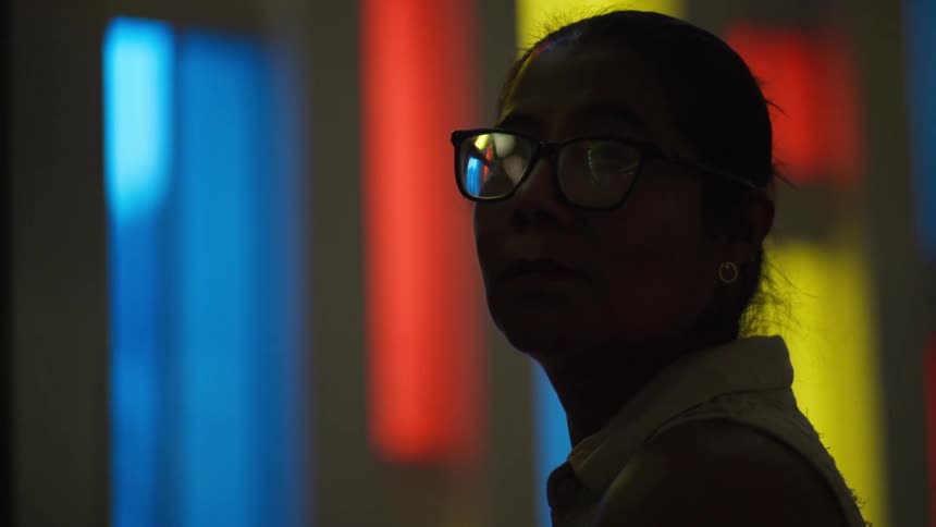 A silhouetted woman wearing glasses slowly turns her head against a vibrant, colorful abstract background