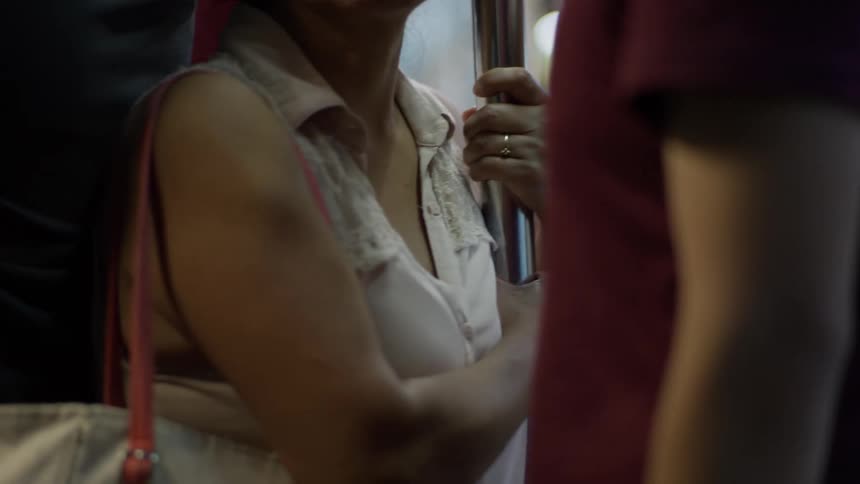 A woman holds onto a metal pole while commuting on a crowded train at night