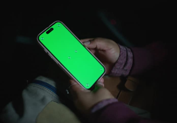 A woman holds a smartphone with a green screen while traveling as a passenger in a car at night