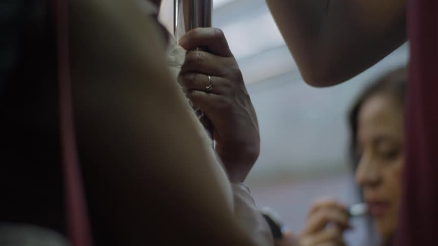 A close-up shot of a woman's hand holding a pole for stability on a shaky, crowded subway train