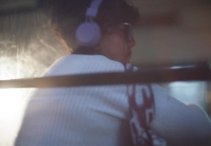 A young student wearing headphones boards a bus and settles in for their commute, as seen from the outside window