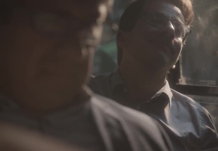 Close-up of a contemplative man with glasses smiling as he rides a bus during a hazy golden hour
