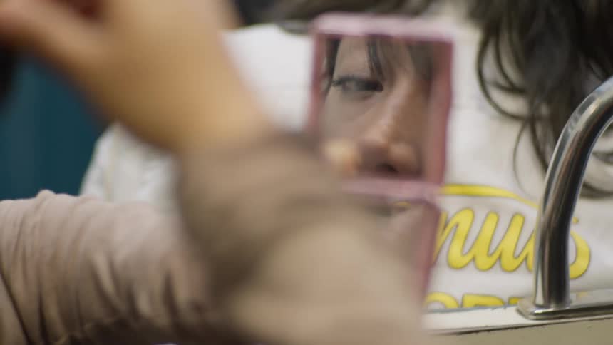 Close-up on a woman's reflection in a compact mirror as she applies her makeup during a train commute