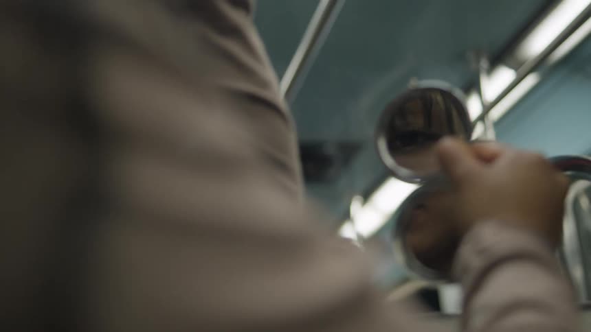 A woman's eye is reflected in a compact mirror as she applies makeup while commuting on a moving train