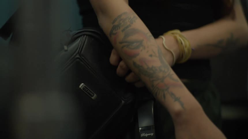 A close-up, handheld shot shows the detailed tattoos on a person's arm while they ride public transport