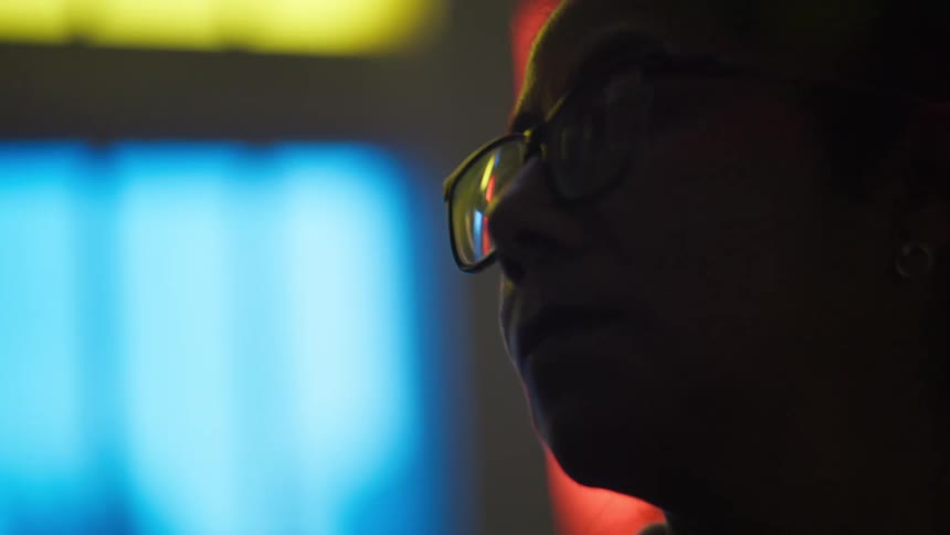 Artistic close-up of a woman's silhouetted face, with red, yellow, and blue lights reflecting in her glasses