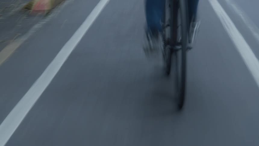 An abstract, motion-blurred, low-angle point-of-view of a person riding a bicycle down a city street