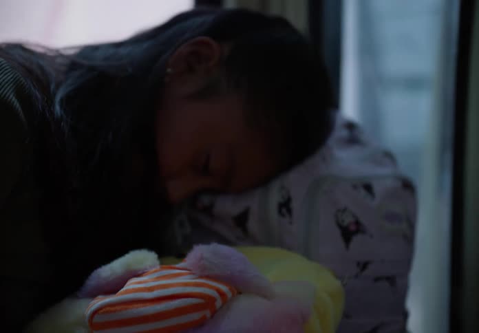 A tired young girl sleeps soundly on her backpack while traveling on a bus