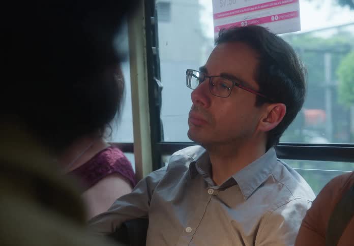 A pensive man wearing glasses looks out the window while commuting on a public bus through the city