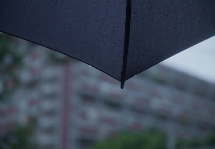 Slow motion close up of raindrops dripping from the edge of a black umbrella on a gloomy day
