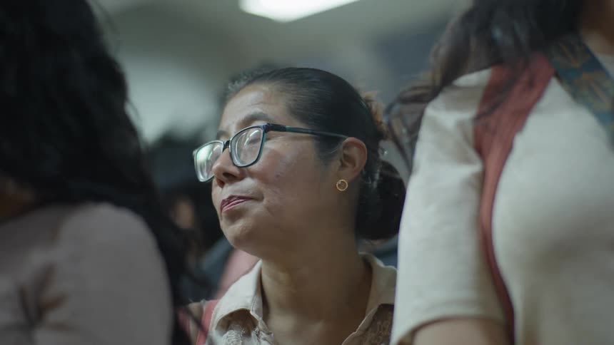 A tired woman with glasses looks around pensively while commuting on crowded public transportation