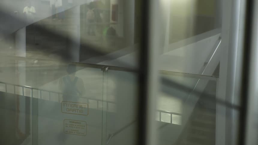 Atmospheric view through a reflective window of a person talking on their phone on a staircase in a modern public building