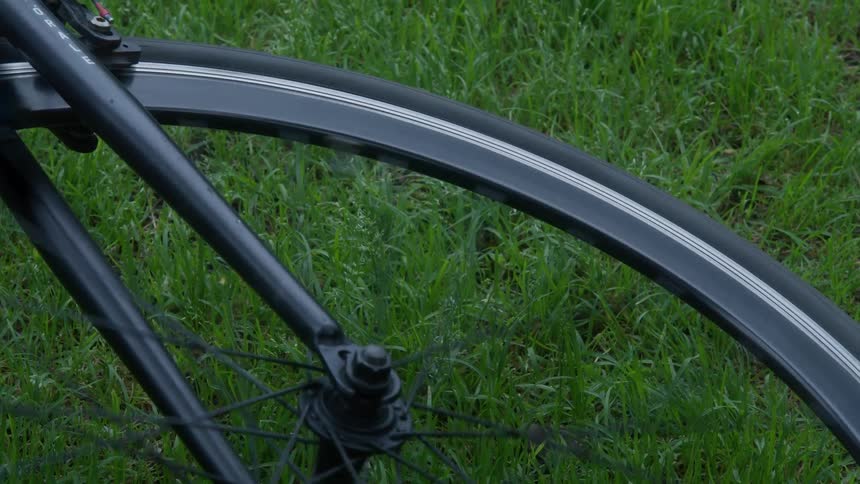 A close-up of a black bicycle wheel spinning slowly to a stop while lying on lush green grass