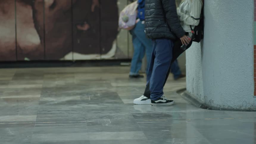 Low-angle shot of a young couple standing close together in a subway station as commuters walk past in slow motion