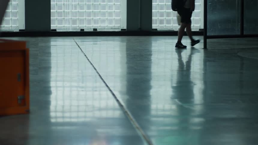 A low-angle view shows the legs and reflections of people walking across a shiny, polished floor in a public space
