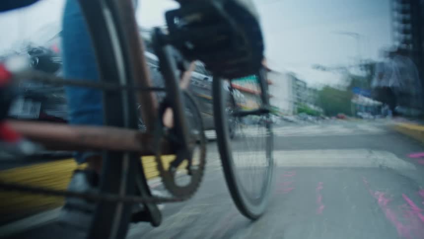 A dynamic low-angle shot follows the spinning wheels of a bicycle as a person pedals down a busy city street