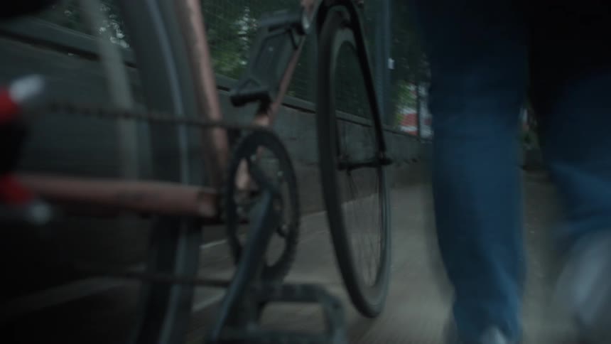 A person walks a bicycle down an urban path, with a close-up on the spinning wheel and pedals