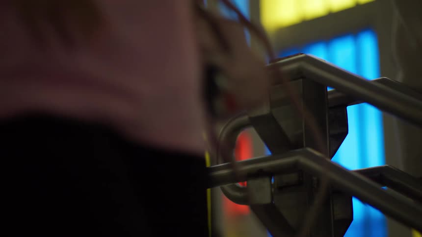 Anonymous commuters walk past a modern handrail set against a colorful wall of lights in a public space