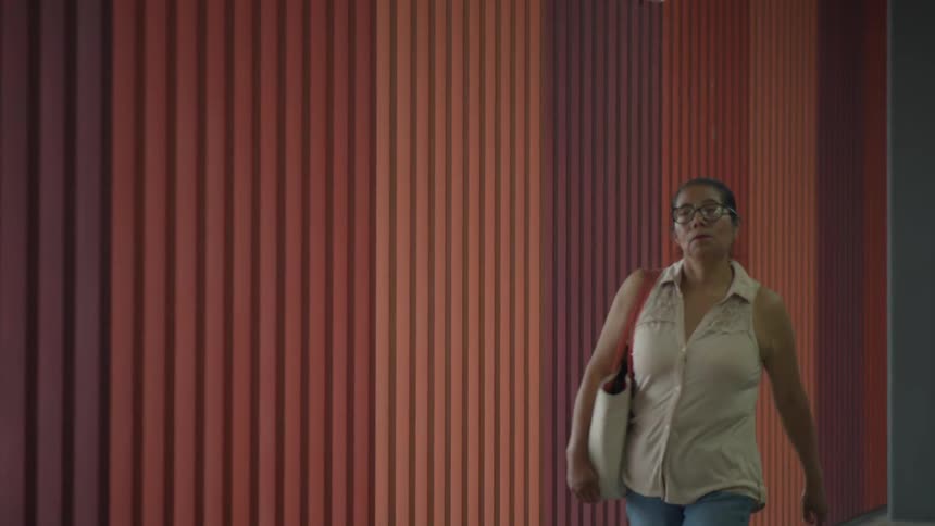 A woman with glasses walks past a vibrant, multi-colored striped wall in slow motion