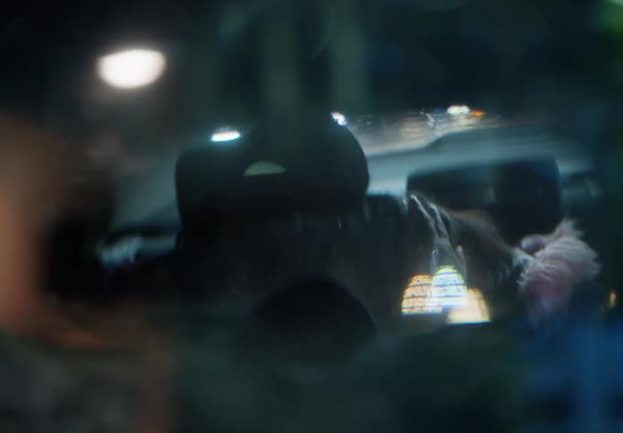 A tender moment between a mother and her sleeping daughter in the backseat of a car is captured through a dreamy rearview mirror at night