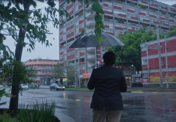 Businessman with an umbrella walks through the rain-soaked city and checks his green-screen phone while waiting to cross the street